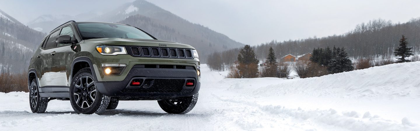 A three-quarter front view of a 2021 Jeep Compass Trailhawk being driven in snow.