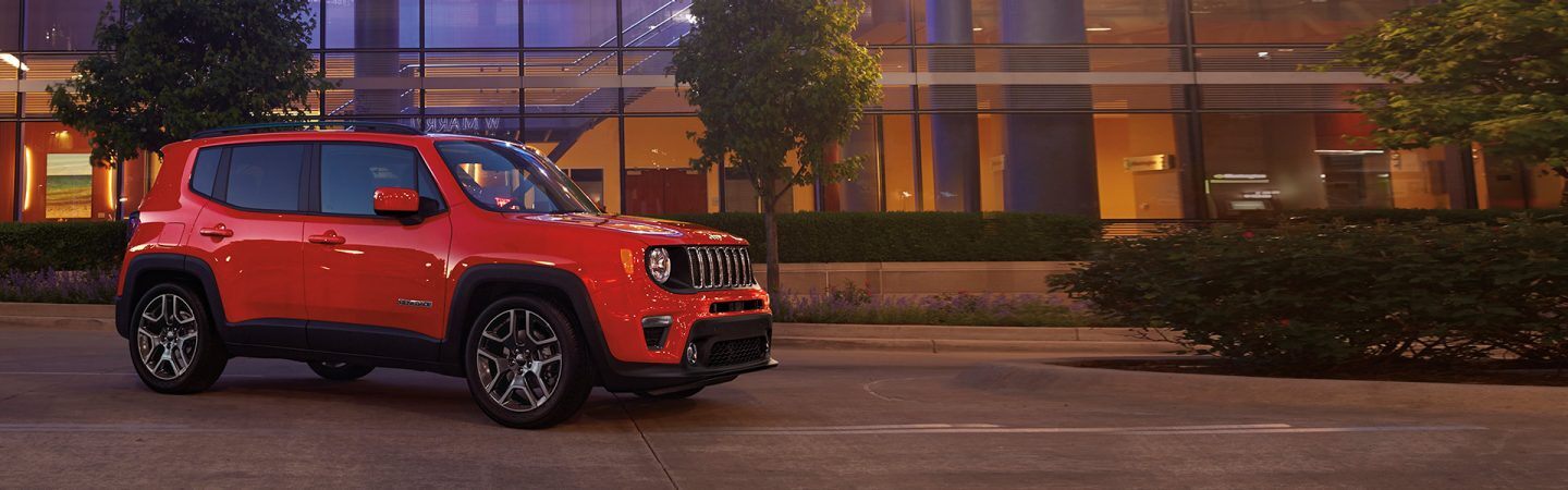 A three-quarter front view of a 2021 Jeep Renegade Latitude parked in front of a building with trees.