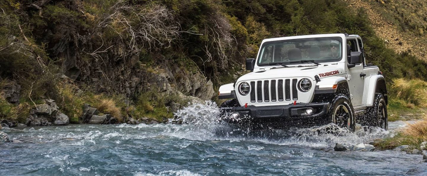 The 2021 Jeep Wrangler Rubicon splashing up water as it's driven across a stream.